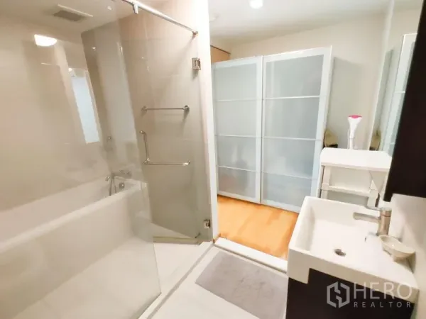 คอนโด ให้เช่าในKhlong Toei, Bangkok - ห้องอาบน้ำกระจกและอ่างอาบน้ำข้างอ่างล้างหน้า มองออกไปยังห้องที่มีประตูบานเลื่อนฝ้าขาว