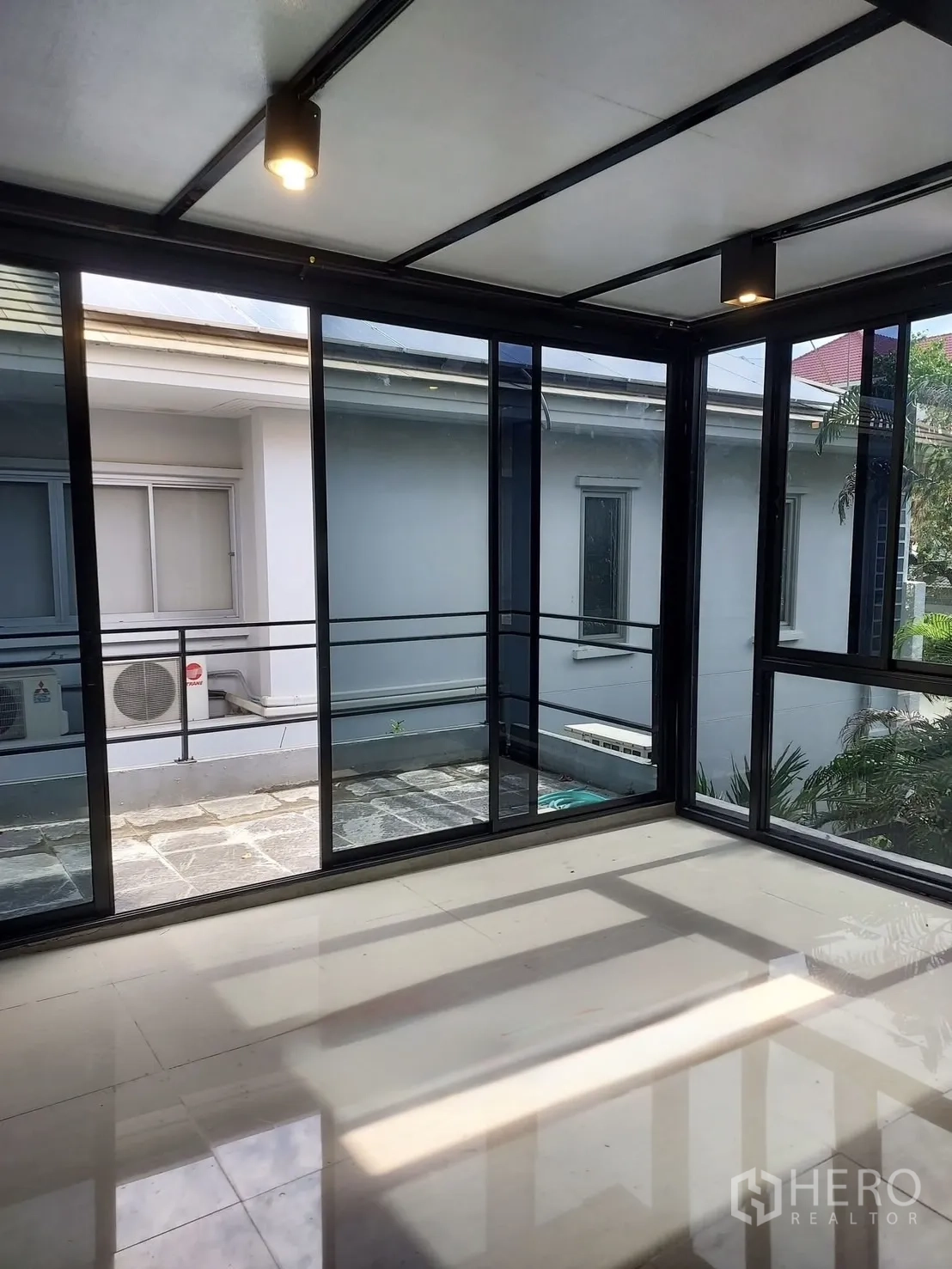 Detached House for rent or sale in Wang Thonglang, Bangkok - Glass-enclosed sunroom with black aluminum frames overlooking a small courtyard.