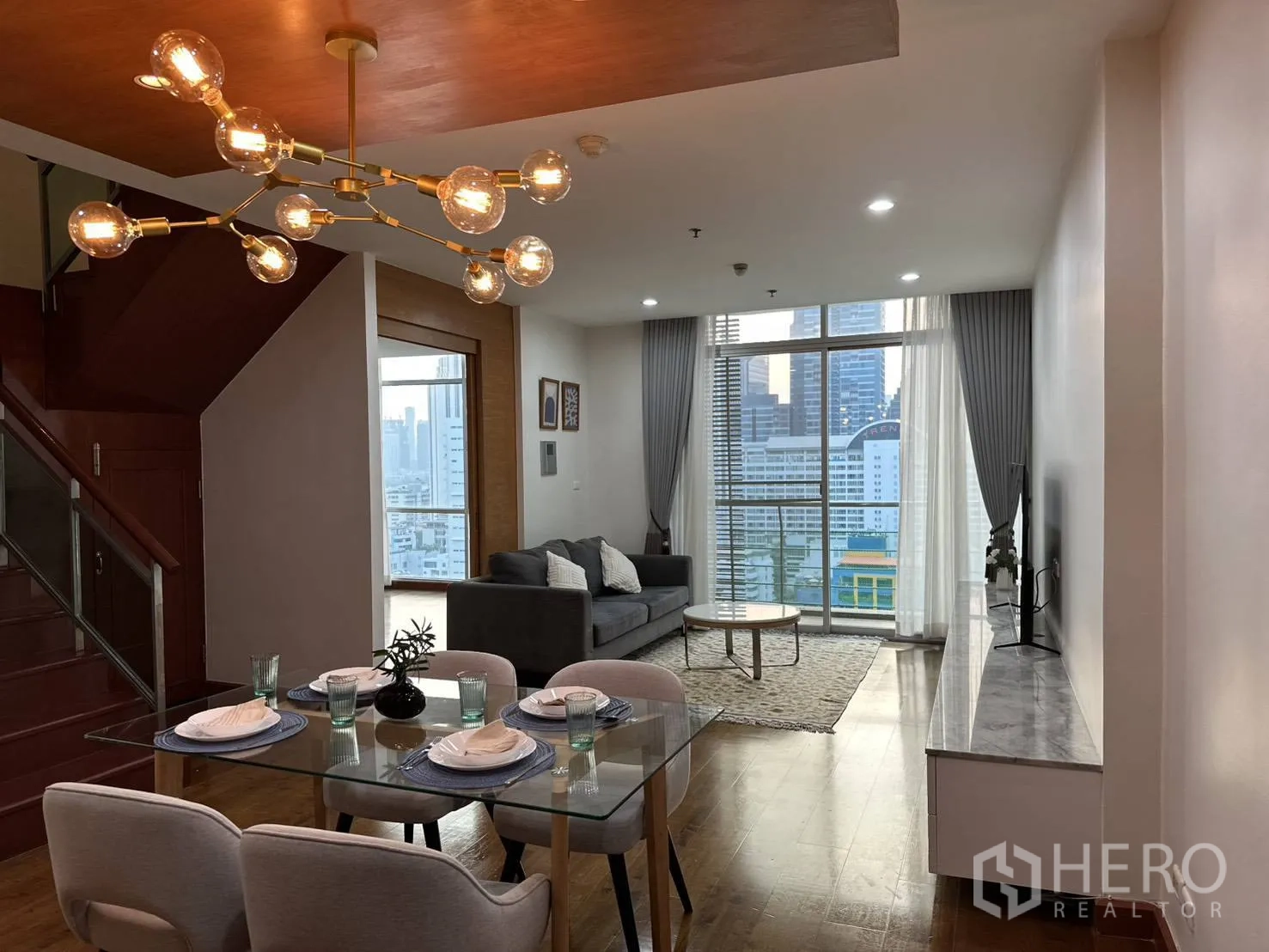 Condominium for rent in Watthana, Bangkok - Open living–dining space with glass table, modern chandelier, and floor-to-ceiling windows.