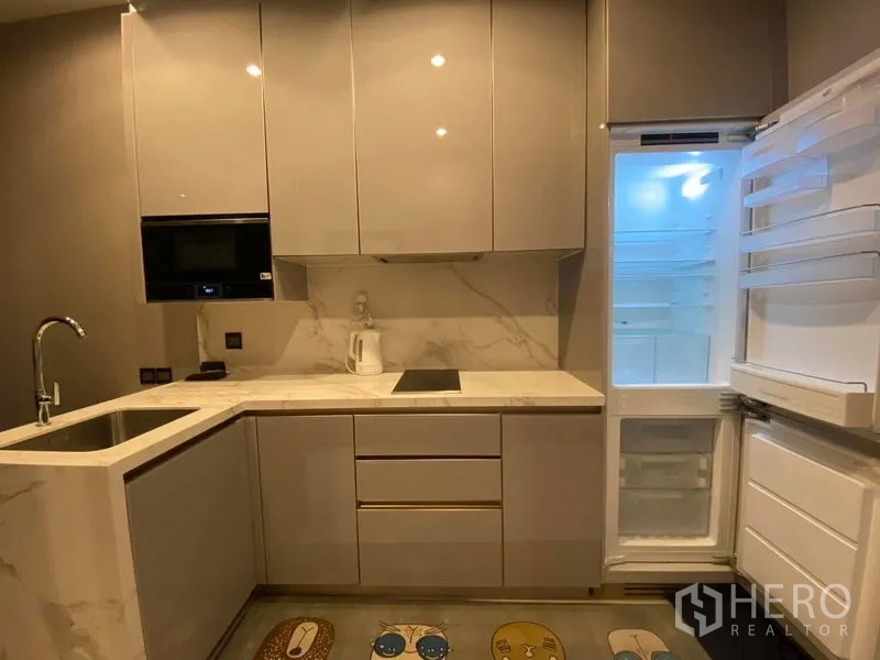 Condominium for rent in Huai Khwang, Bangkok - Compact glossy L-shaped kitchen with induction cooktop, built-in microwave, and an open refrigerator.