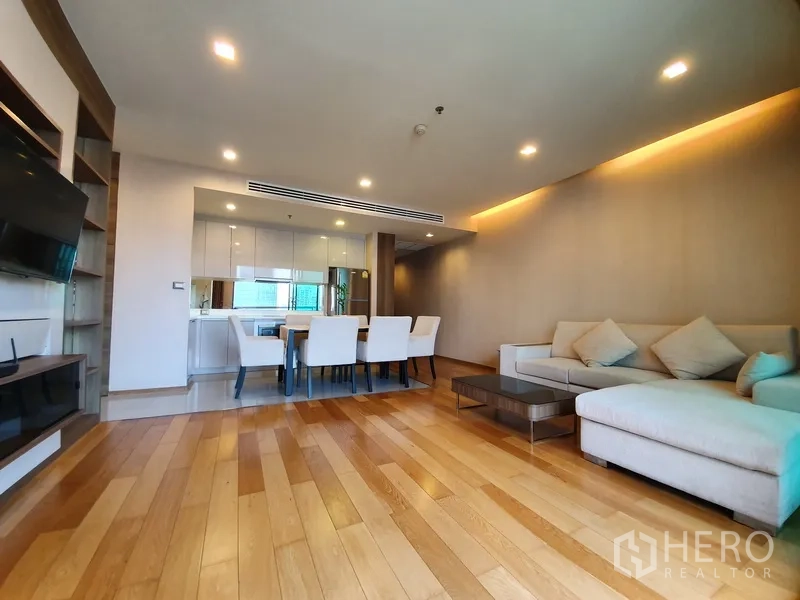 公寓 出租在Bang Rak, Bangkok - 宽敞起居区，木地板与转角沙发，旁接白色厨房和餐桌