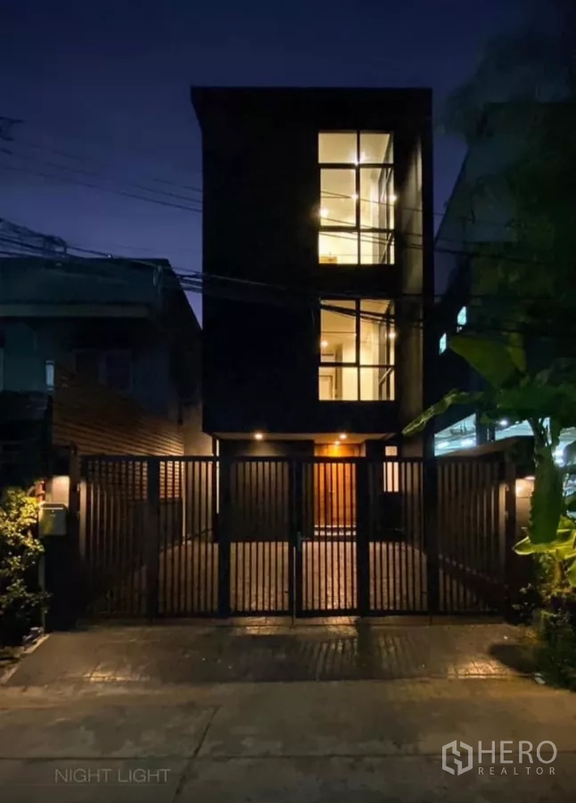 Detached House for rent in Huai Khwang, Bangkok - Modern three-storey detached house facade at night with gated driveway and warm lighting in Huai Khwang.
