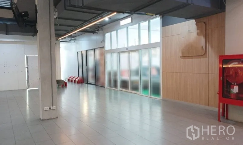 零售空间 出租在Watthana, Bangkok - 宽敞走廊，瓷砖地面、磨砂玻璃店面、木质墙面与红色消防柜。