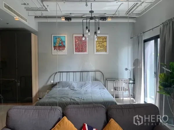 Condominium for sale in Watthana, Bangkok - View of the bedroom through a glass partition from the sofa, with artwork above the bed and large windows.