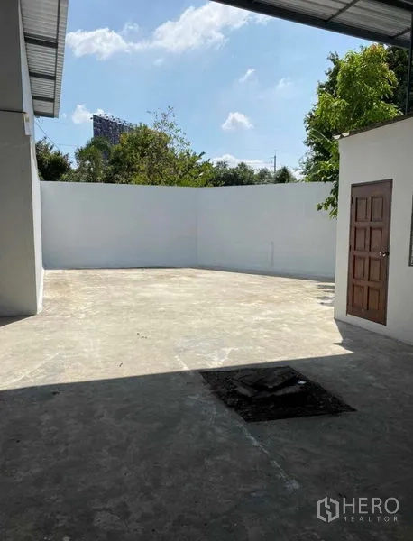 货栈 出租在Bang Khen, Bangkok - 室外硬化院子，白色高墙与小门，蓝天可见