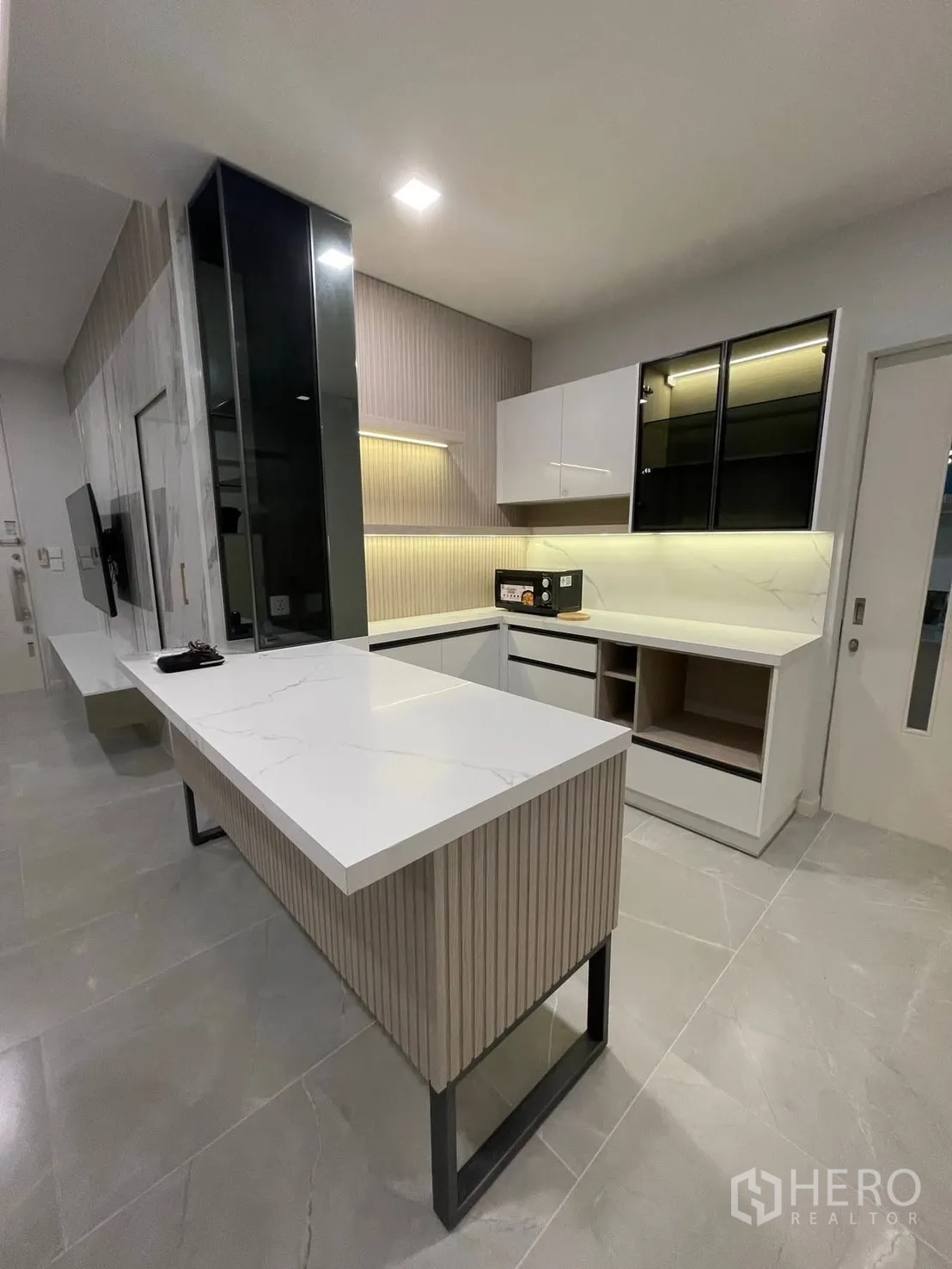Detached House for rent in Prawet, Bangkok - Sleek kitchen with long peninsula, white countertops, and illuminated cabinets.