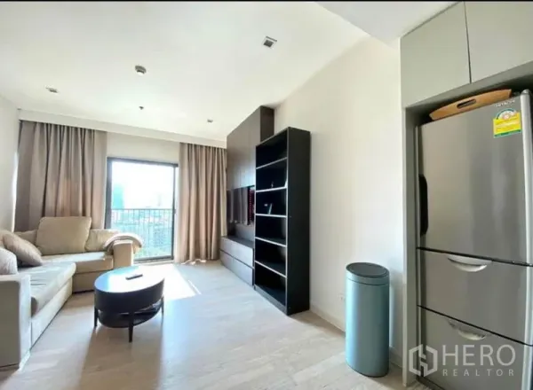 คอนโด ให้เช่าในKhlong Toei, Bangkok - ห้องนั่งเล่นโซฟาสีเบจ พร้อมผนังทีวีและชั้นวาง ใกล้หน้าต่างออกระเบียง