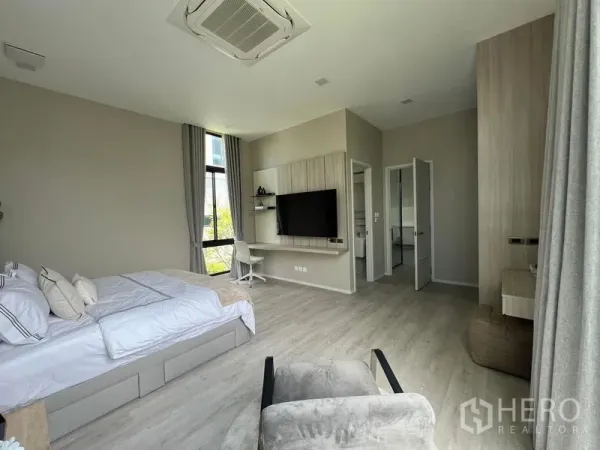 Detached House for rent in Saphan Sung, Bangkok - Primary bedroom with built-in desk, wall-mounted TV and entrance to an ensuite bathroom.