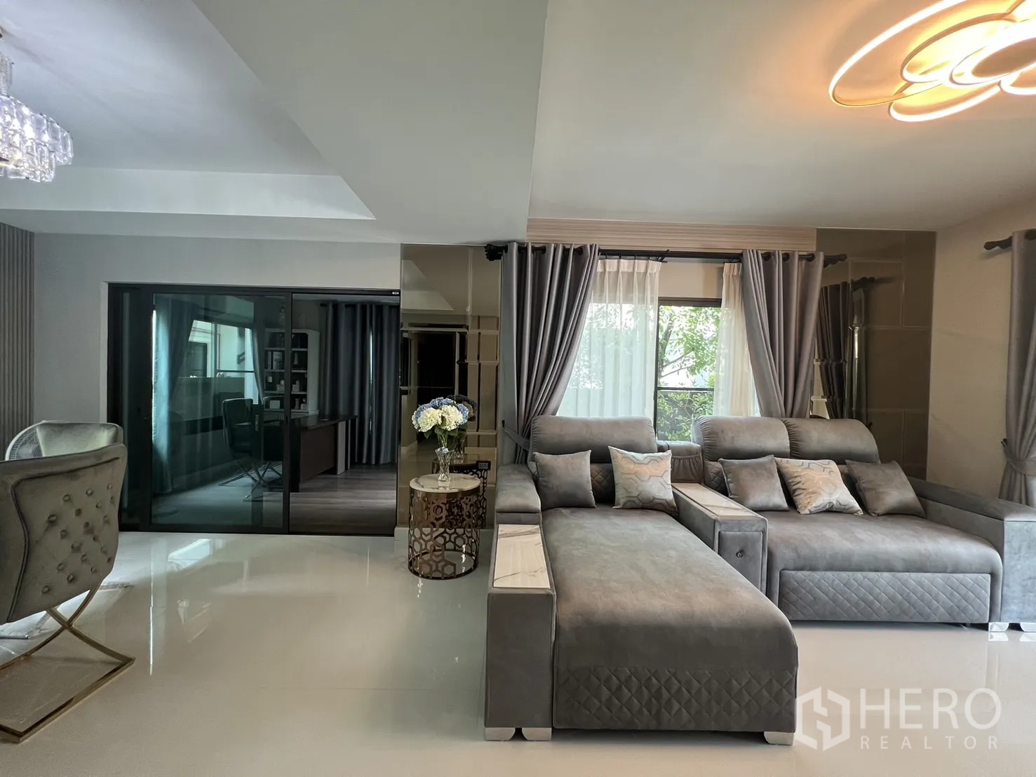 Detached House for rent in Bang Phli, Samut Prakan - Spacious living room with large gray sectional sofa and floor-to-ceiling windows.