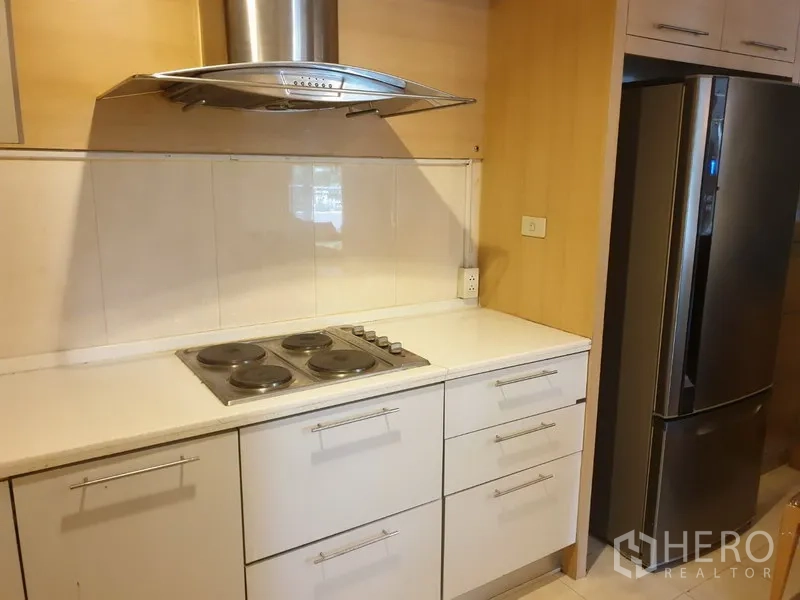 Condominium for rent in Watthana, Bangkok - Modern kitchen with electric cooktop, stainless hood, white cabinets, and large fridge.