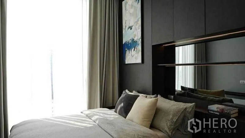Condominium for rent or sale in Watthana, Bangkok - Bedroom with dark feature wall, artwork and mirrored shelf by the window.