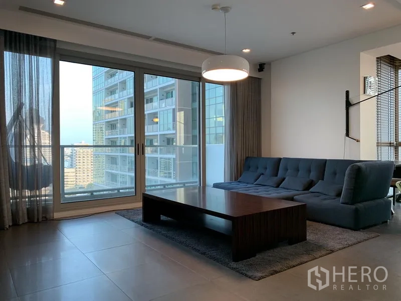 Condominium for rent or sale in Khlong San, Bangkok - Bright living room with floor-to-ceiling windows, gray sofa and balcony overlooking Bangkok skyline at The River.
