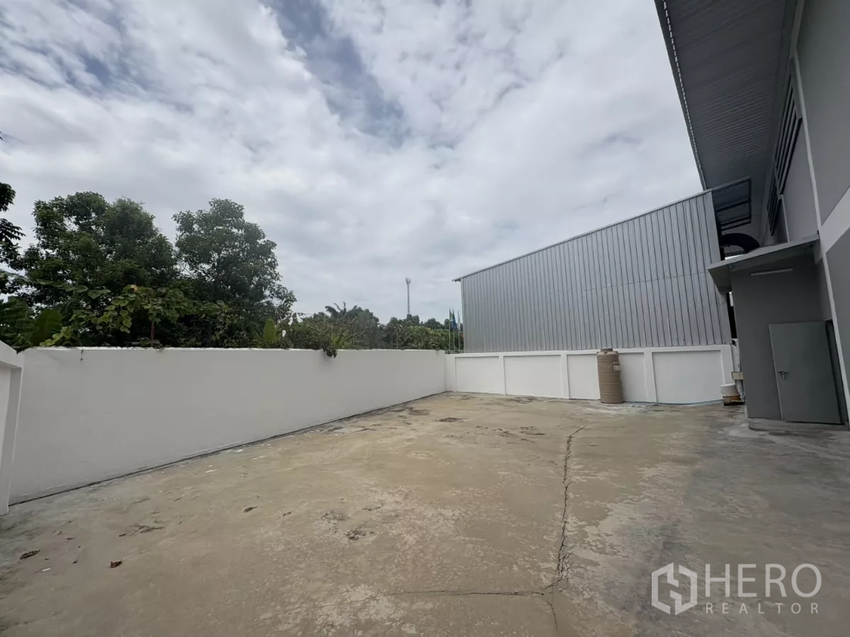 Factory for rent in Phra Samut Chedi, Samut Prakan - Rear service yard beside metal-clad wall and water tank storage.