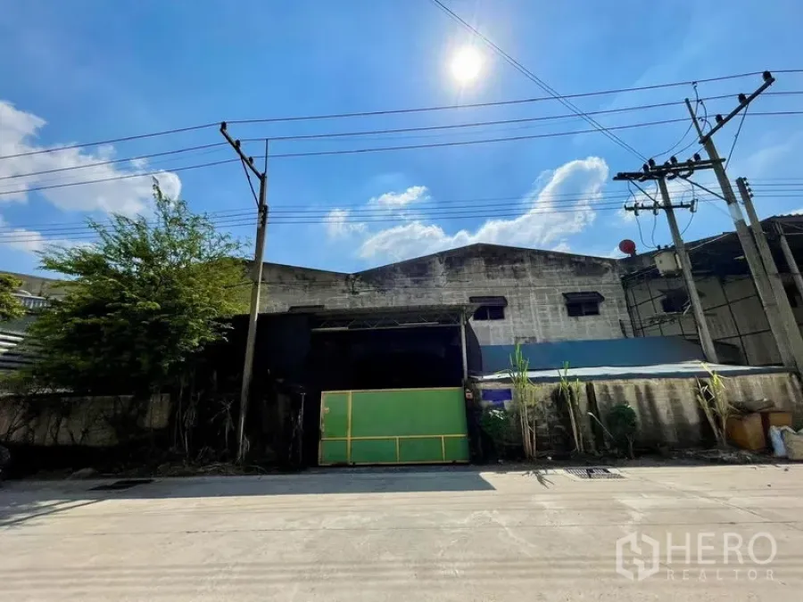 Warehouse for rent in Krathum Baen, Samut Sakhon - Front exterior of the industrial warehouse with green sliding gate, boundary wall and overhead power lines.