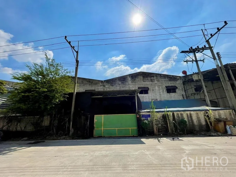 Warehouse for rent in Krathum Baen, Samut Sakhon - Front exterior of the industrial warehouse with green sliding gate, boundary wall and overhead power lines.