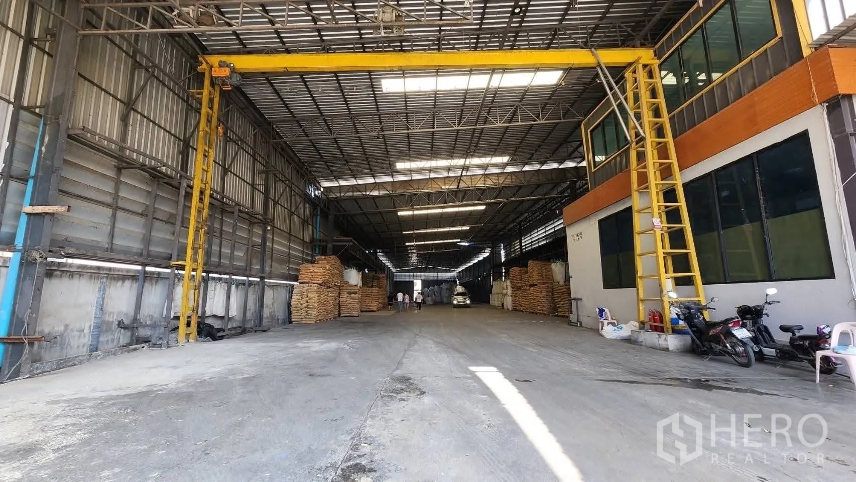 仓库 for rent in Bang Phli, Samut Prakan - 仓库中轴通道笔直，设有吊轨与堆放物料，屋顶照明下可见车辆。