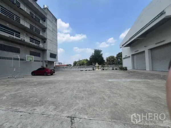 Warehouse for rent in Lam Luk Ka, Pathum Thani - Large concrete yard with multiple roller-shutter loading bays and parking beside the warehouse building in Lam Luk Ka.