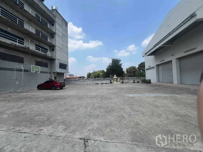 Warehouse for rent in Lam Luk Ka, Pathum Thani - Large concrete yard with multiple roller-shutter loading bays and parking beside the warehouse building in Lam Luk Ka.