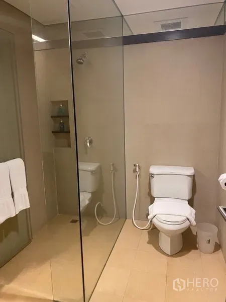 Apartment for rent in Khlong Toei, Bangkok - Modern bathroom featuring a glass-enclosed shower, toilet and light-toned tiles.
