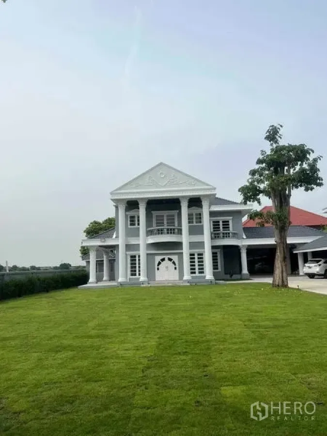 Detached House for sale in Bang Na, Bangkok - Daytime facade of a neoclassical detached house with four columns and a large lawn.