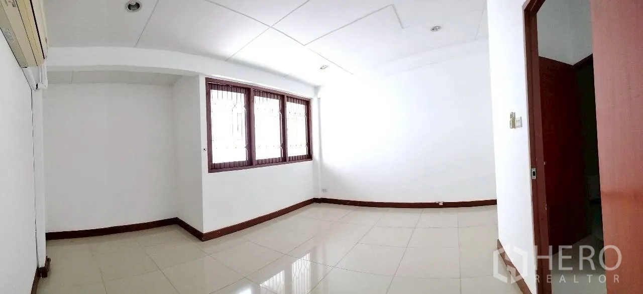 Home Office for rent in Watthana, Bangkok - Large white-tiled room with window grilles and doorway to bathroom.