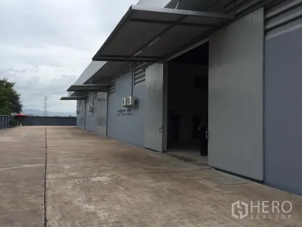 คลังสินค้า ให้เช่าในSi Racha, Chon Buri - ลานขนถ่ายด้านนอก ประตูบานสไลด์โลหะขนาดใหญ่ มีกันสาด และพื้นคอนกรีตสำหรับรถบรรทุก
