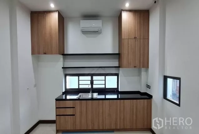 Home Office for rent in Watthana, Bangkok - Secondary pantry kitchen with wood cabinets, black counter, window sink and wall‑mounted air conditioner.