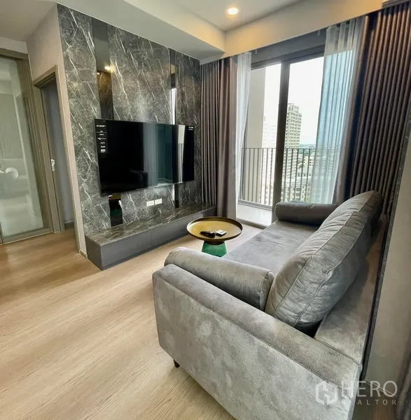 Condominium for rent in Samut Prakan - Living area with wall-mounted TV on a marble feature and sliding doors to the balcony.