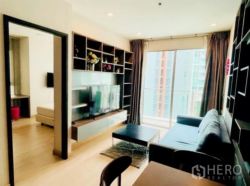 Condominium for rent - Bright living room with built-in shelving, TV unit, sofa, and floor-to-ceiling balcony doors.