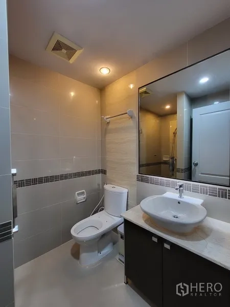 Condominium for rent in Phra Khanong, Bangkok - Tiled bathroom with wide mirror, vessel sink vanity, and toilet.