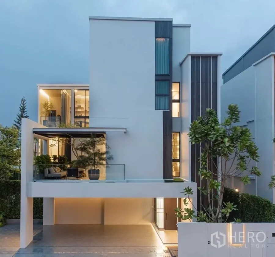 独立式住宅 出租在Saphan Sung, Bangkok - 现代三层独栋别墅外观，带遮蔽车位与玻璃露台，傍晚灯光。