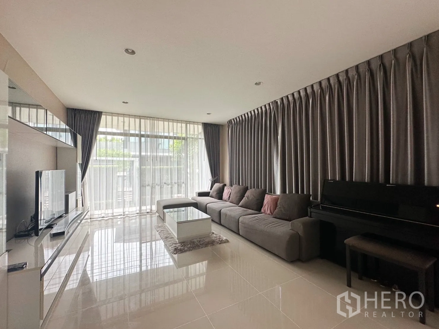 Detached House for rent or sale in Bang Kapi, Bangkok - Bright living room with long sectional sofa, TV wall and upright piano.