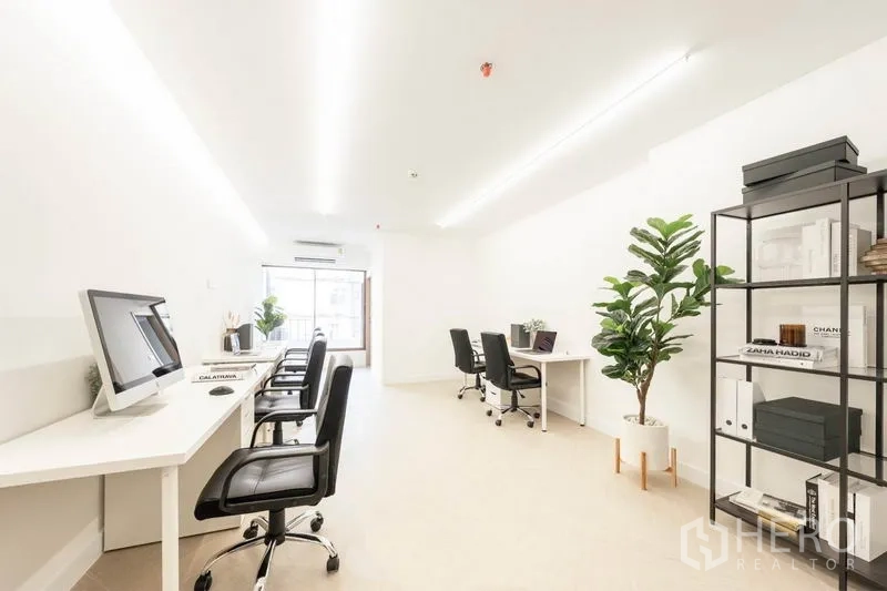 Office Space for rent in Khlong Toei, Bangkok - Light-filled office corridor with multiple workstations, computers, indoor plants and a large window at the end.