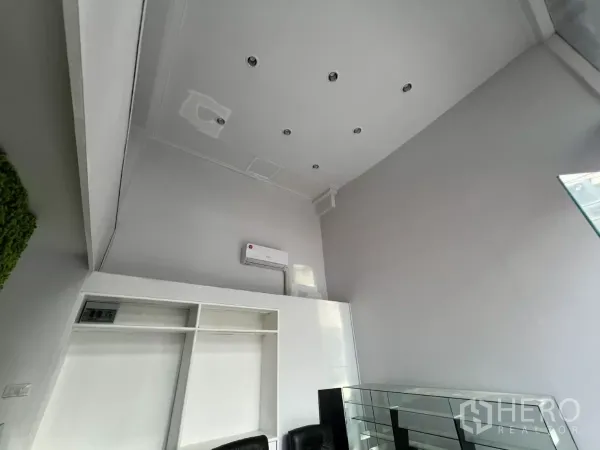 พื้นที่ขายปลีก ให้เช่า - มุมเงยเห็นเพดานสูงสีขาว ไฟดาวน์ไลท์ และเครื่องปรับอากาศ