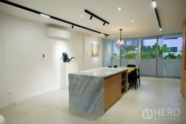 Home Office for rent in Phra Khanong, Bangkok - Open-plan living and dining space with marble island, track lighting and sliding glass doors to a leafy balcony.