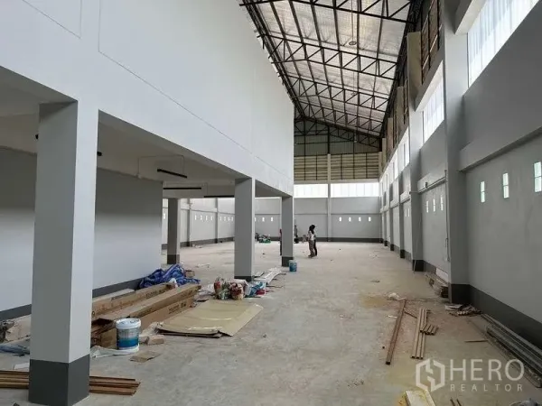 Factory for sale in Khlong Luang, Pathum Thani - Wide factory bay with interior columns, tall windows and construction materials on the floor.