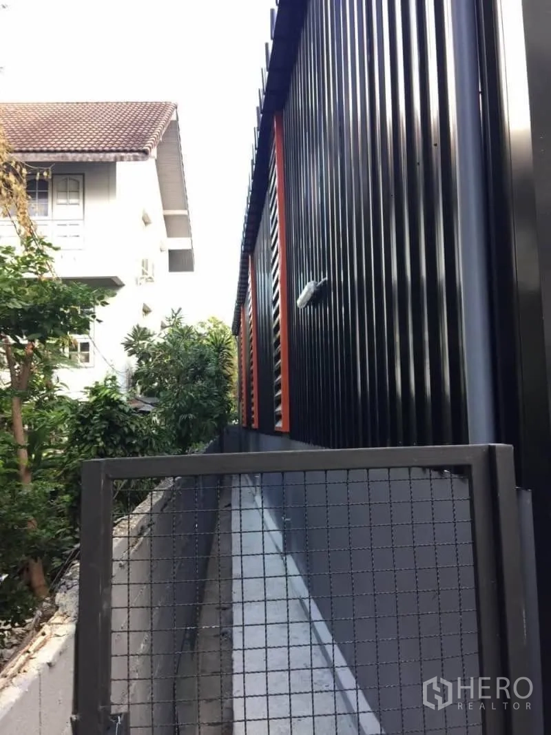 Warehouse for rent in Lat Phrao, Bangkok - Narrow side walkway beside the warehouse with fencing and greenery.