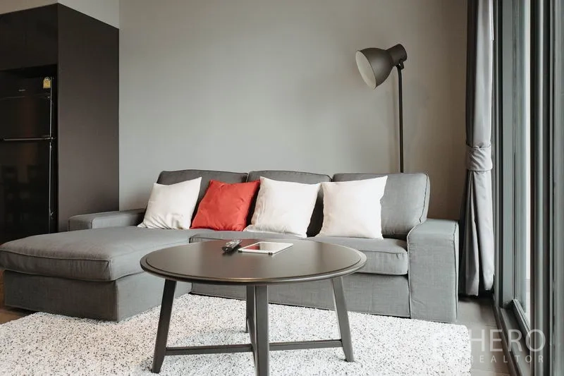 Condominium for rent in Watthana, Bangkok - Grey L-shaped sofa with colorful cushions beside floor-to-ceiling windows.