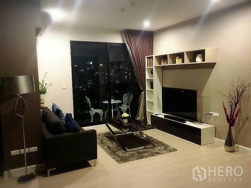 Condominium for rent or sale in Huai Khwang, Bangkok - Cozy lounge at night with TV unit, coffee table and balcony city views.