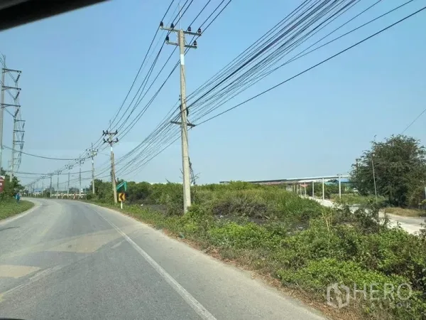 Land for sale in Mueang Samut Sakhon, Samut Sakhon - Road curve with utility poles next to a green, undeveloped land parcel.
