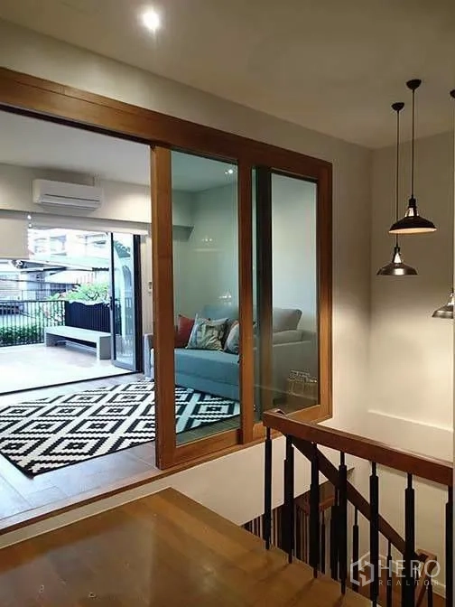 Townhouse for rent in Watthana, Bangkok - View from staircase to living area with large glass doors and balcony.