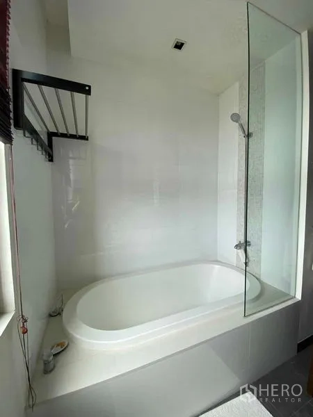 Condominium for rent in Yan Nawa, Bangkok - Bathroom with oval soaking bathtub and glass shower screen by a window.