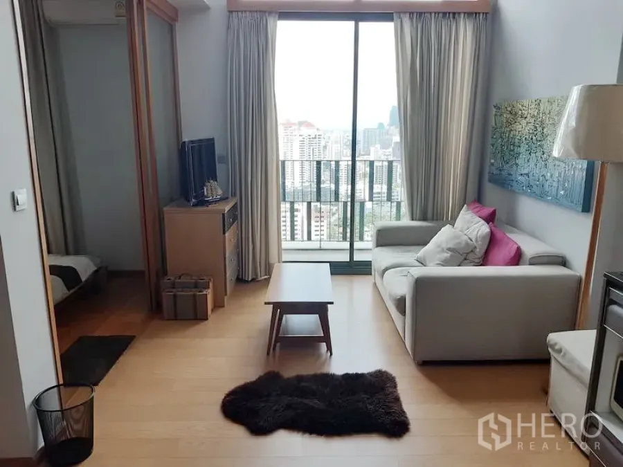Condominium for rent in Khlong Toei, Bangkok - Bright living room with sofa and TV opening to a balcony with Bangkok city views.