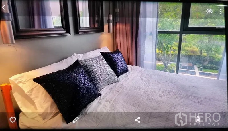 Condominium for rent in Phra Khanong, Bangkok - Close‑up of bed facing picture window with greenery and pool deck view.