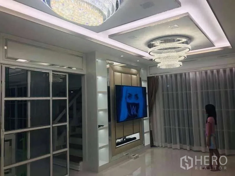 独立式住宅 出租在Chom Thong, Bangkok - 客厅带嵌入式吊顶灯与水晶吊灯，墙挂电视，空间现代明亮。
