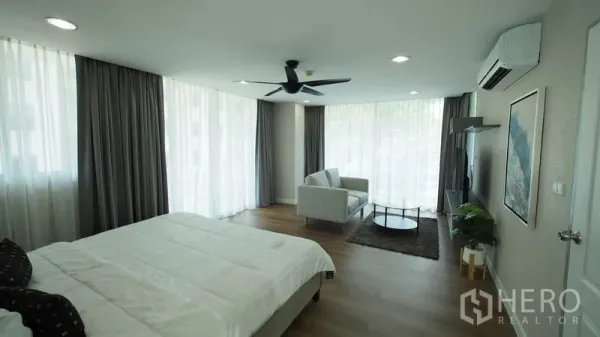 คอนโด ให้เช่าในKhlong San, Bangkok - ห้องมาสเตอร์มุมสว่าง ผ้าม่านสูงจรดเพดาน ชุดโซฟา และผนังสื่อบันเทิง