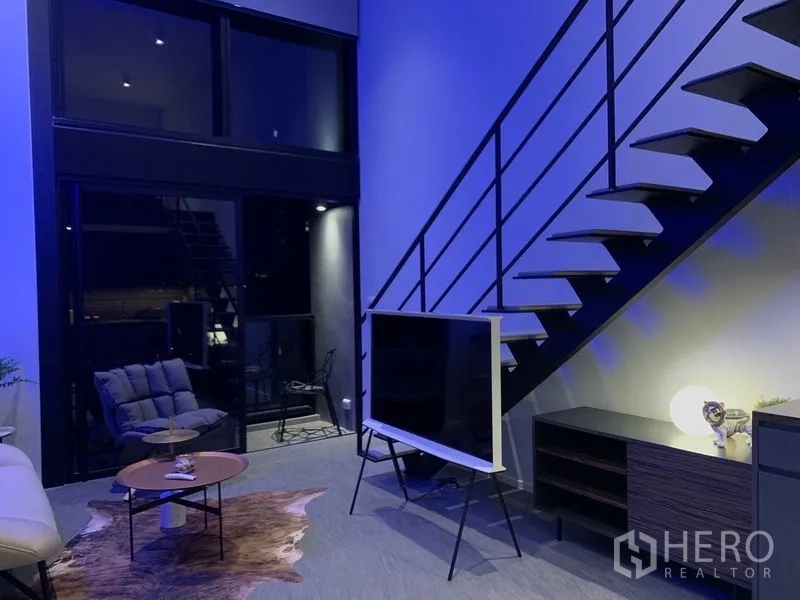 公寓 出租在Bang Rak, Bangkok - 双层挑高客厅，金属楼梯、电视与落地窗。