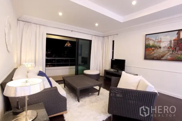 คอนโด ให้เช่าในSathon, Bangkok - ห้องนั่งเล่นสว่างตกแต่งด้วยโซฟาหวาย พรมสีขาว และประตูกระจกสไลด์ออกสู่ระเบียงวิวสกายไลน์กรุงเทพฯ ยามค่ำคืน