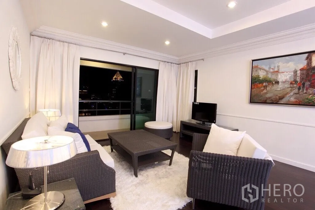 คอนโด ให้เช่าในSathon, Bangkok - ห้องนั่งเล่นสว่างตกแต่งด้วยโซฟาหวาย พรมสีขาว และประตูกระจกสไลด์ออกสู่ระเบียงวิวสกายไลน์กรุงเทพฯ ยามค่ำคืน