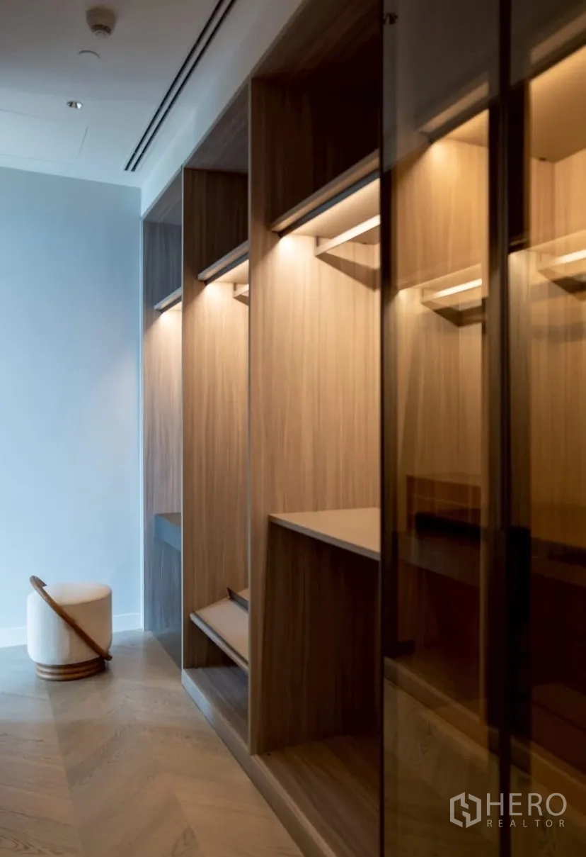 公寓 出租或出售在Pathum Wan, Bangkok - 步入式衣帽间，木质开放格架与玻璃柜门照明。